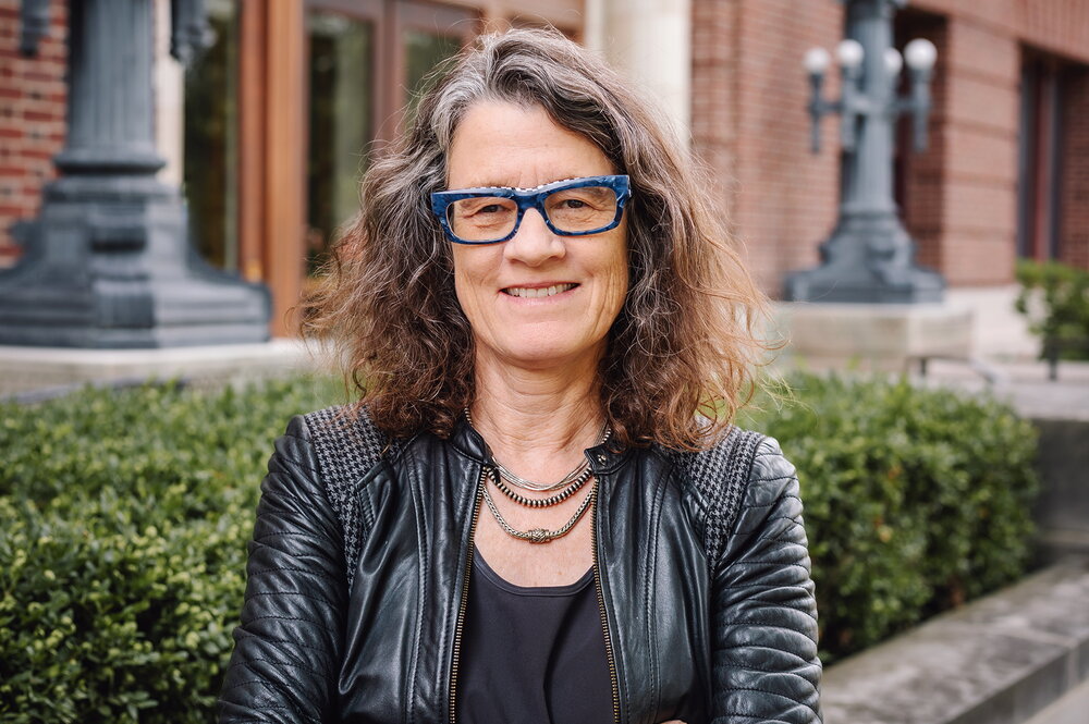 Leslie Reagan in a black leather jacket stands outside of a university building.
