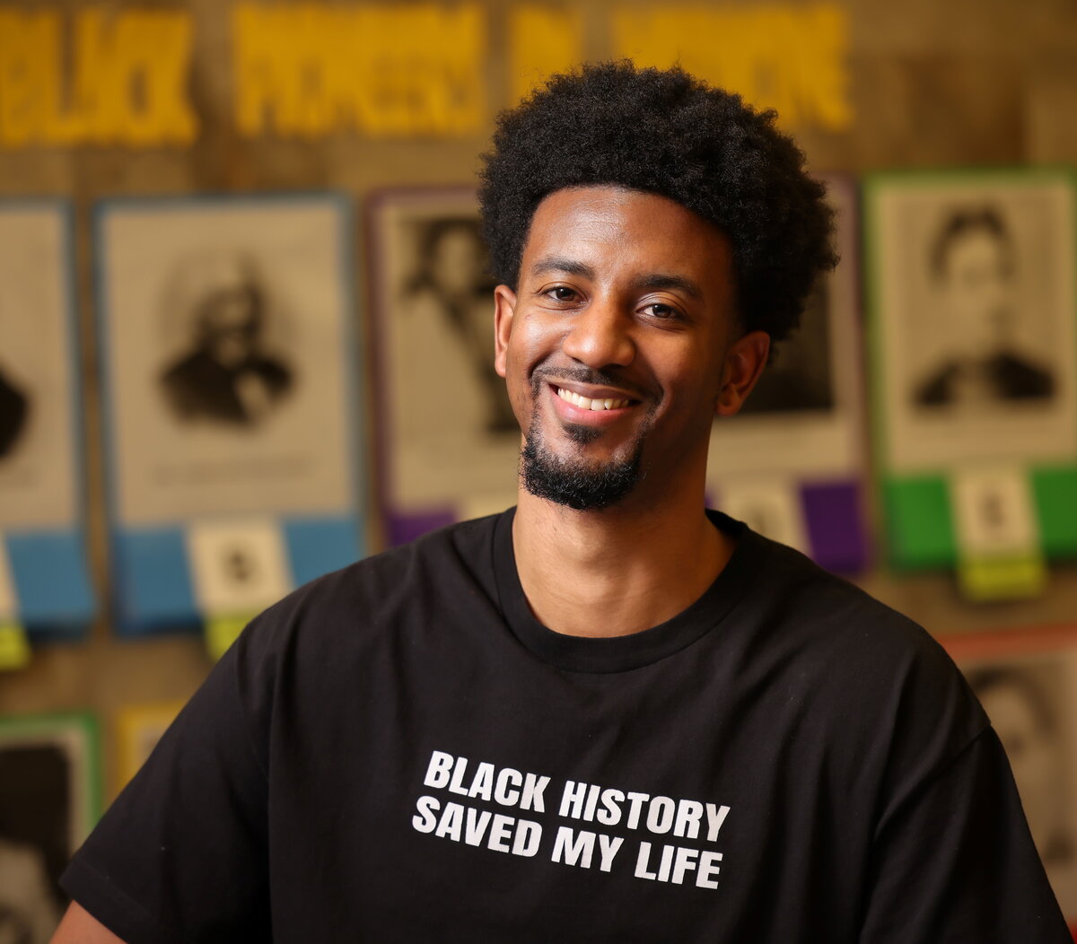 Ernest Crim in front of a bulletin board wearing a black t-shirt that says Black history saved my life.