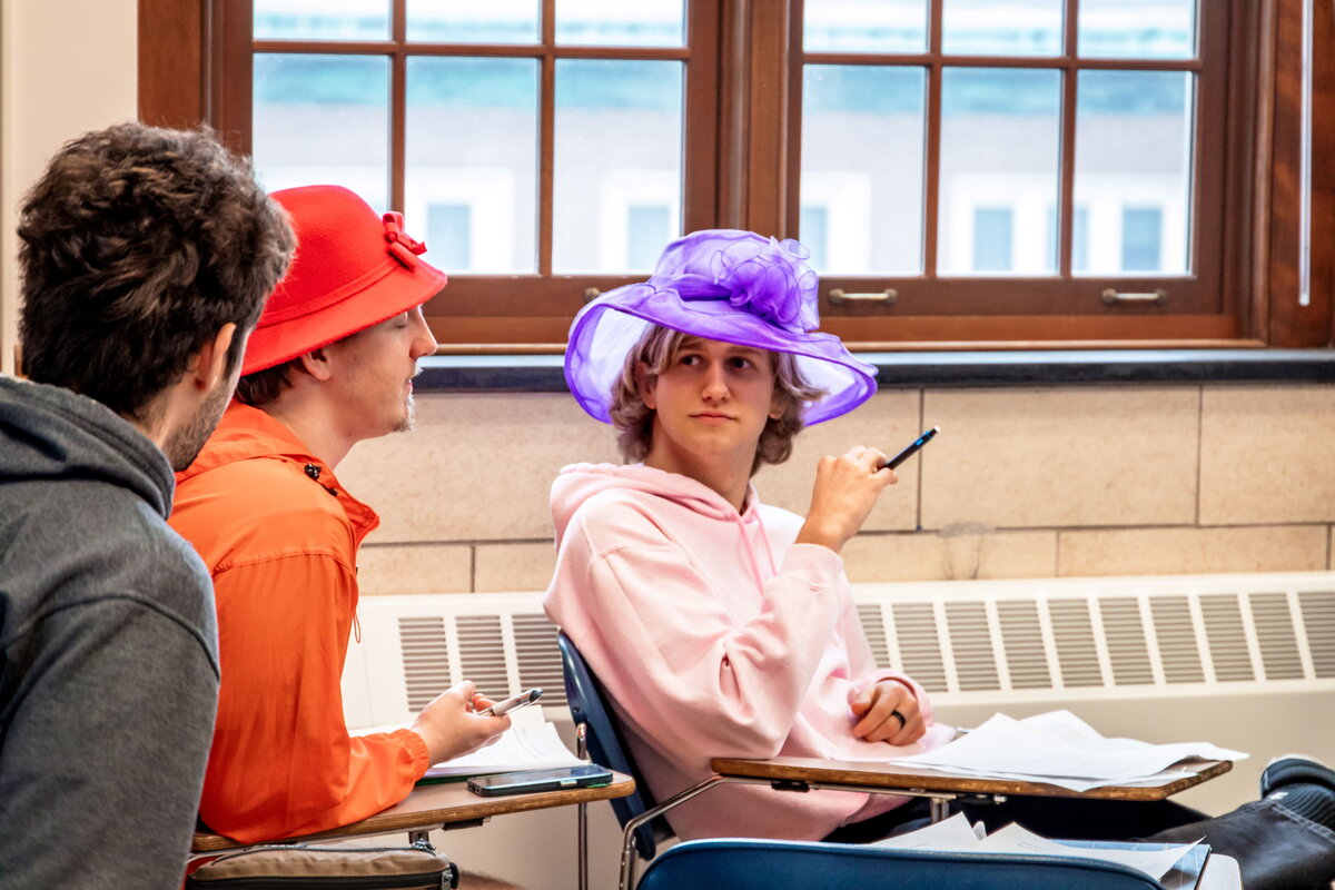 Students in gregory hall, one student wears a purple hat.