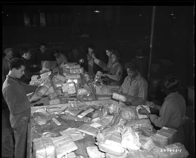 Men and women sorting mail and packages at a large overflowing table.