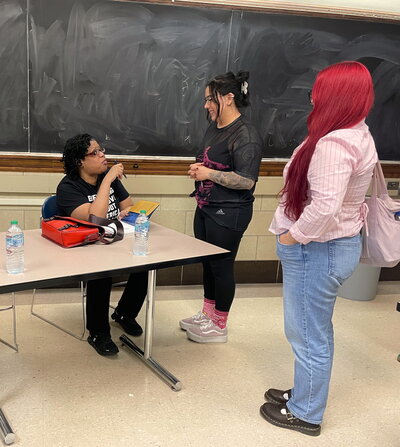 Mikki Kendall signs books at a table while talking to two students.