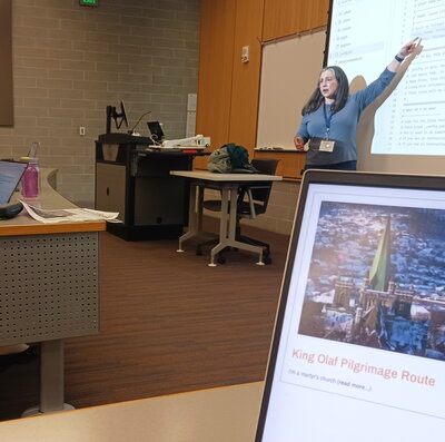 Kalani Craig stands at the front of the room pointing at a screen.
