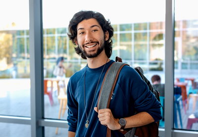 Student in front of windows holding backpack.