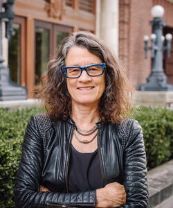 Leslie Reagan in a black leather jacket stands outside of a university building.