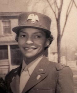 Margaret E. Barnes in her WAC uniform. A house and tree and behind her.