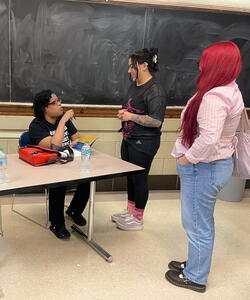 Mikki Kendall signs books at a table while talking to two students.