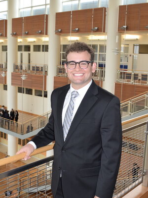 Noam stands in an academic building in a suit