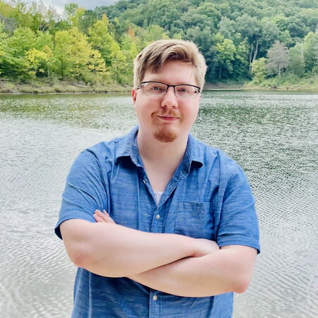 Austin Justice with his arms crossed in front of a lake.