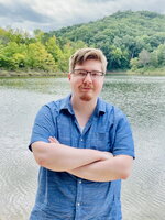 Austin Justice with his arms crossed in front of a lake.